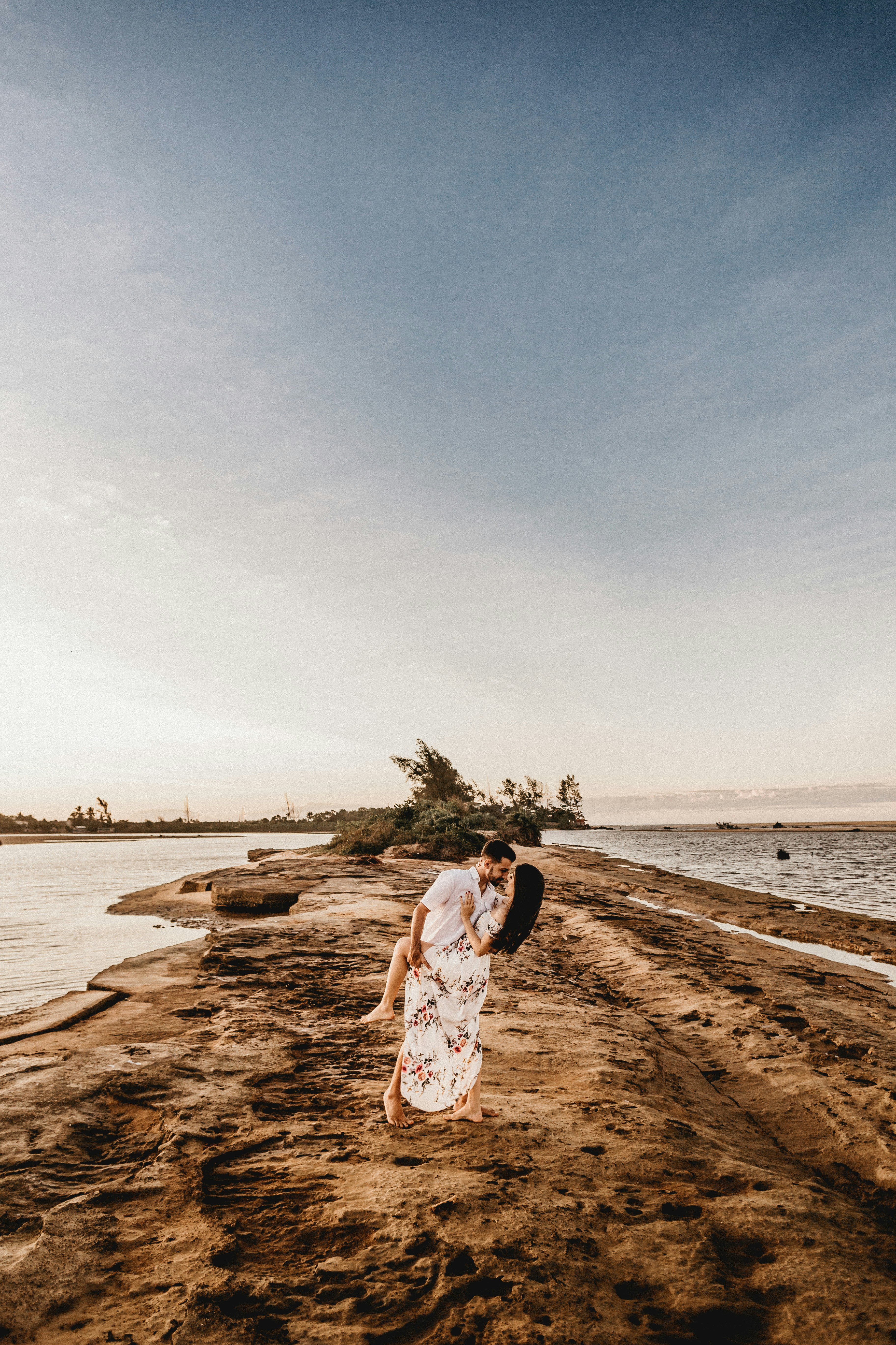 woman in white and brown dress standing on brown sand near body of water during daytime